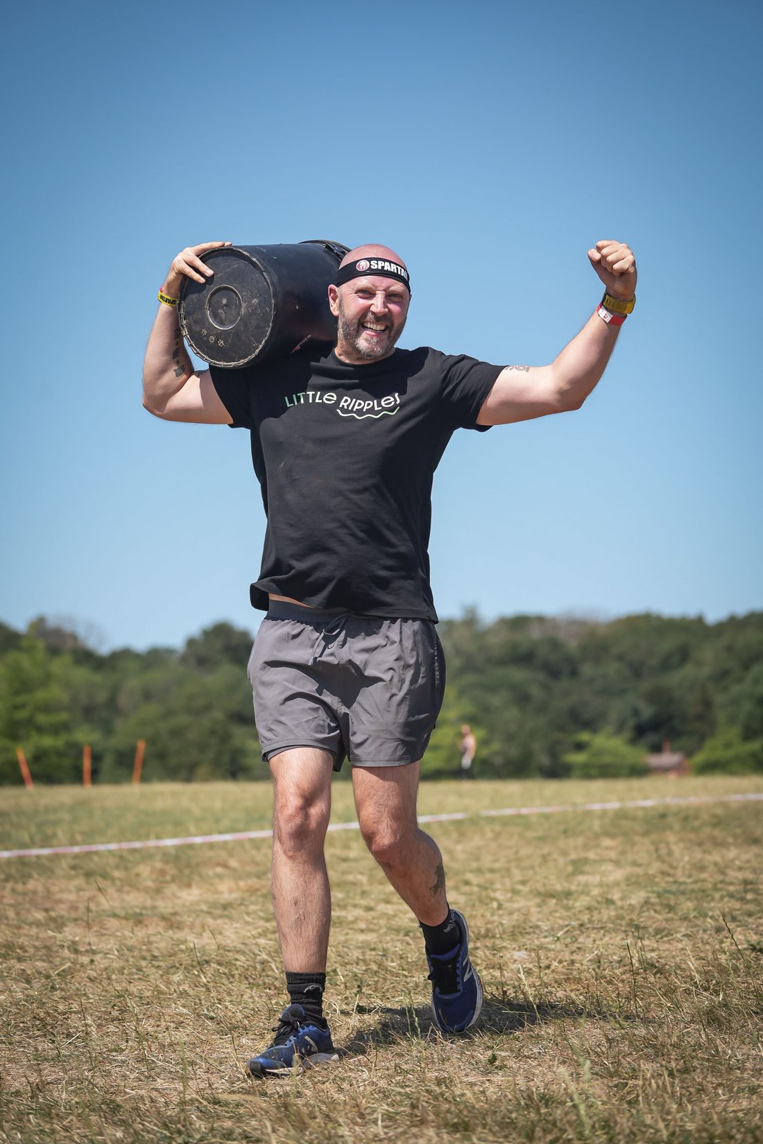 A Little Ripples supporter carrying a weighted bucket during an obstacle race, arm raised in celebration