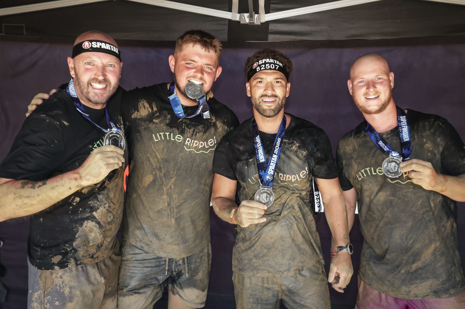 Four mud-covered Little Ripples supporters holding up their finisher medals